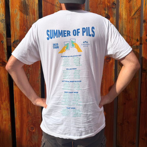 Person wearing a white t-shirt with 'Summer of PILS' text and graphics on the back, standing against a wooden fence.