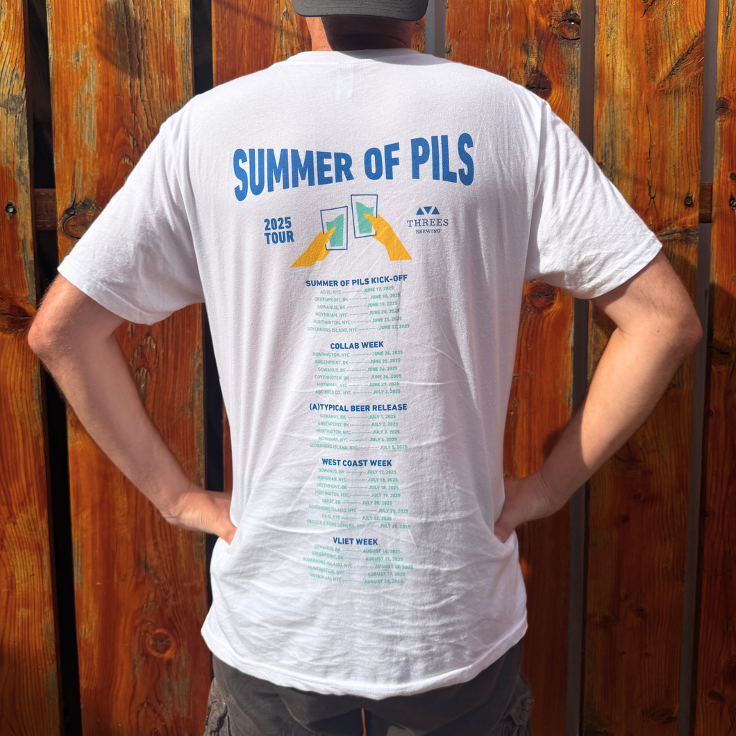 Person wearing a white t-shirt with 'Summer of PILS' text and graphics on the back, standing against a wooden fence.