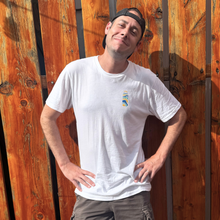 Load image into Gallery viewer, Man wearing a white t-shirt with a logo standing against a wooden fence.
